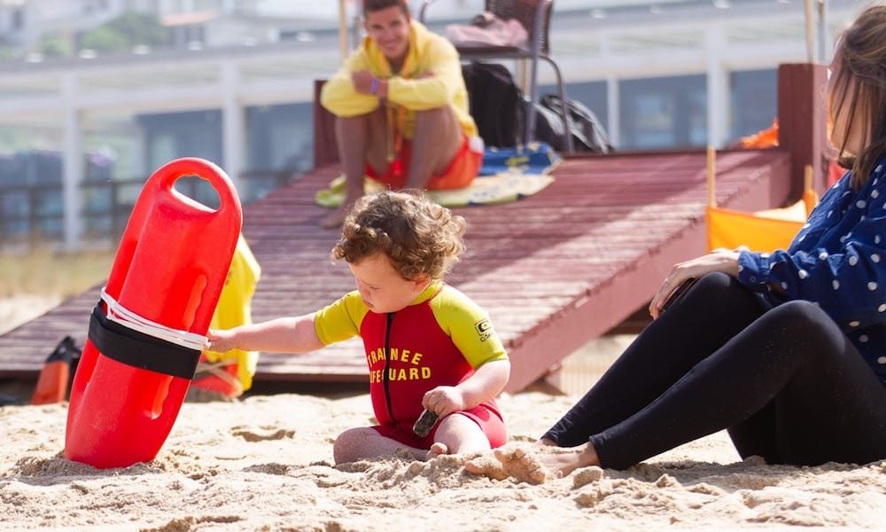 Toddler playing with safety equipment on Foz do Lizandro beach while the family is watching