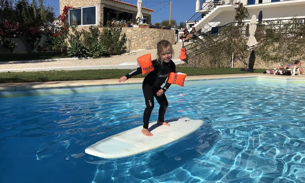 Kid is having fun on a surfboard in the pool while the family is watching
