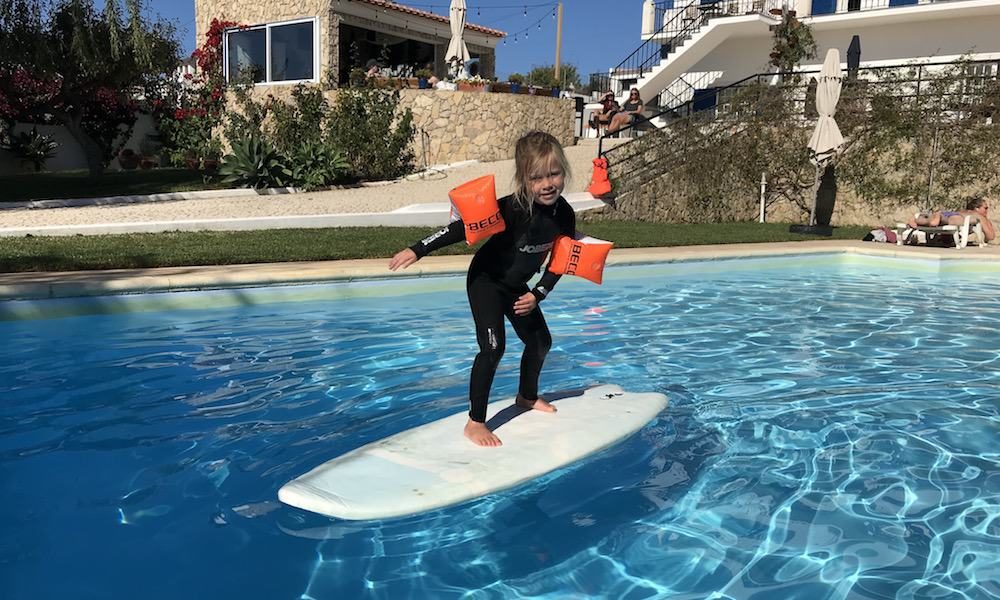 Kid is having fun on a surfboard in the pool while the family is watching